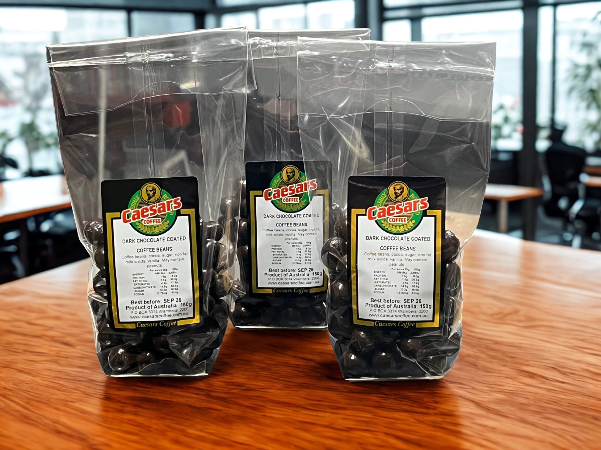 Dark Chocolate Coated Coffee Beans retail packs on a wooden table with a blurred indoor background